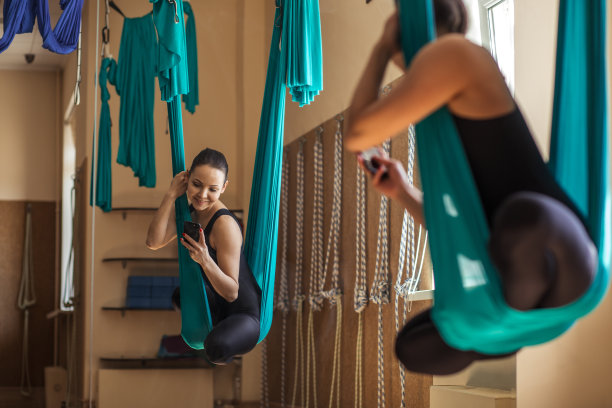 一个有吸引力的女运动员用手机挂在吊床上的背影照片。图片下载