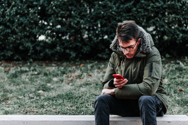 一个年轻人坐在户外玩智能手机图片下载