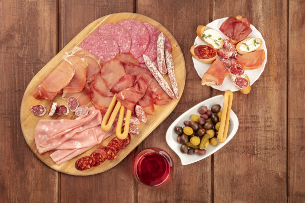 美味的熟食店。这是一张从上方拍摄的照片，上面有许多不同的香肠、火腿和冷切肉，背景是乡村的黑色，还有一杯红酒和一个地方的文字图片下载