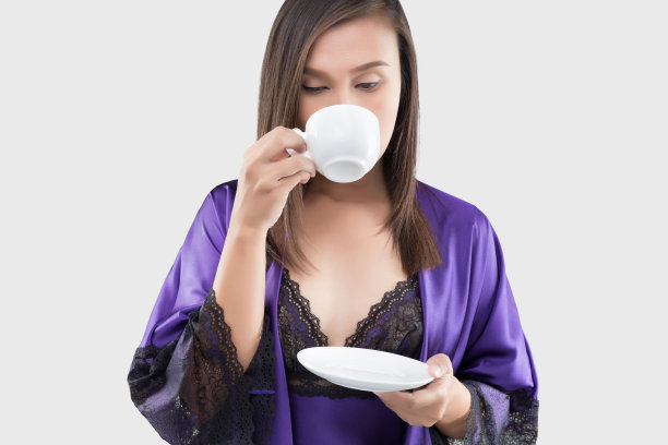 一个迷人的女人的肖像在紫色睡衣和丝绸长袍举着白色的茶在一个白色的背景，女人在缎子睡衣喝咖啡，女士在紫罗兰美丽的睡衣，早上好图片下载