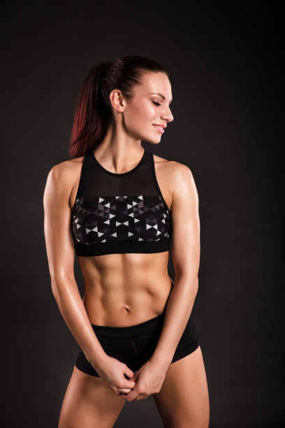 强壮的女性健美运动员有完美的腹肌，肩膀，二头肌，三头肌和胸部。照片上的运动年轻女子在黑色的背景。图片下载