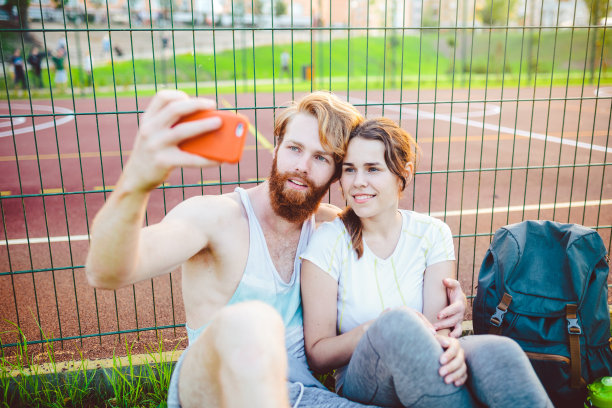 一个长着红头发和胡子的欧洲男人和一个在户外运动后休息的女人。这个人伸出一只红色的智能手机，用航天飞机的前置摄像头拍了一张照片图片下载
