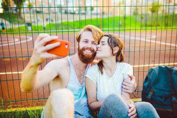 一个长着红头发和胡子的欧洲男人和一个在户外运动后休息的女人。这个人伸出一只红色的智能手机，用航天飞机的前置摄像头拍了一张照片图片下载