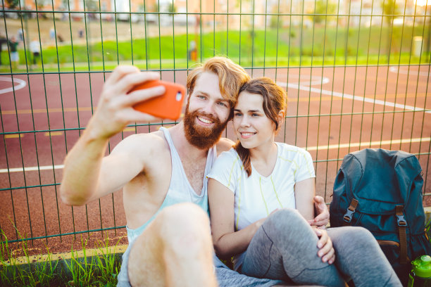 一个长着红头发和胡子的欧洲男人和一个在户外运动后休息的女人。这个人伸出一只红色的智能手机，用航天飞机的前置摄像头拍了一张照片图片下载