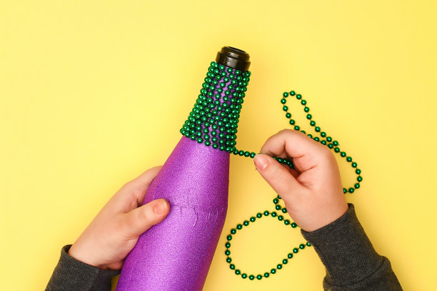 Diy Mardi Gras瓶子，紫色胶纸，绿色珠子，狂欢节面具，亮片黄色背景。图片下载