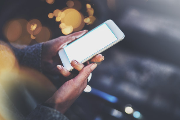 女人握着智能手机在夜晚大气的城市。女性的手在用手机。模糊背景的特写。耀斑,散景效果。图片下载