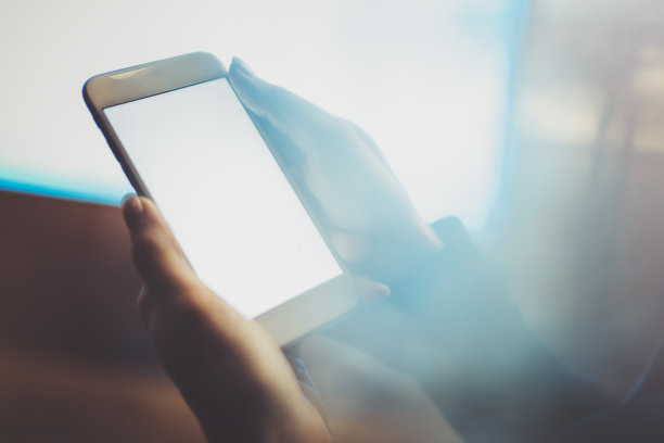 女孩拿着智能手机与白色空屏幕在夜晚大气的城市。模糊背景的特写。图片下载