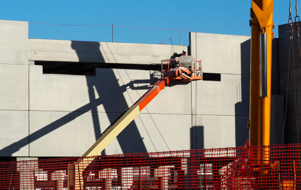 在一座在建的新建筑的未加工混凝土外立面上，一名工人在高空采伐樱桃的平台上工作图片下载