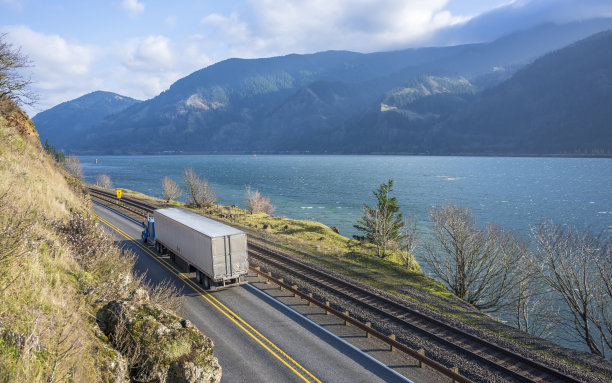 带冰箱半挂车的大卡车行驶在狭窄的道路上，道路两旁有悬崖和河流图片下载