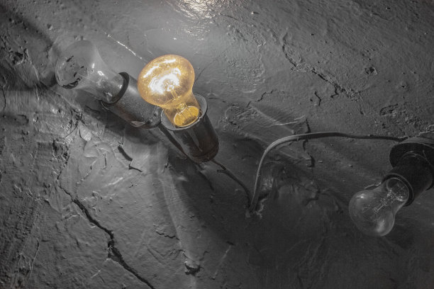 在涂了漆的水泥墙的背景上，闪烁着又脏又旧的灯泡图片下载