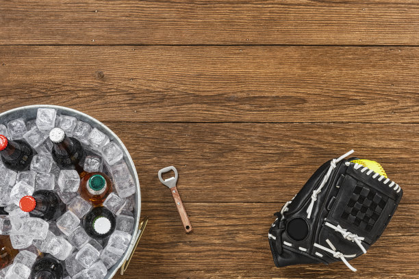 俯视着放在木桌上的垒球手套，上面有垒球和各式各样的啤酒瓶，放在镀锌桶里冰上图片下载