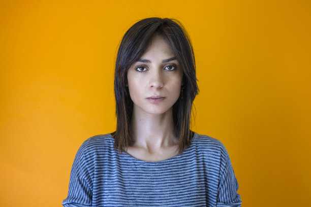 面部表情:一个愤怒的棕色头发的年轻女子，黄色背景图片下载