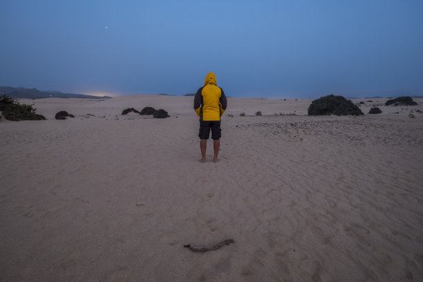 晚上，身穿黄色夹克的单身男子站在corralejo Fuerteventura沙漠中间等待。寒冷和享受周围的自然，没有人替代度假和生活理念图片下载