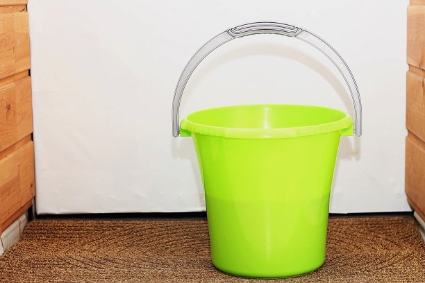 清洁用的绿色塑料桶放在门边的棕色垫子上。图片下载