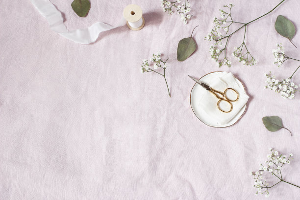 风格的库存图片。女性化的婚礼桌面场景。婴儿的呼吸吉普赛花，干绿色桉树叶，缎带，金色剪刀在粉红色的亚麻背景。空的空间。前视图。图片下载