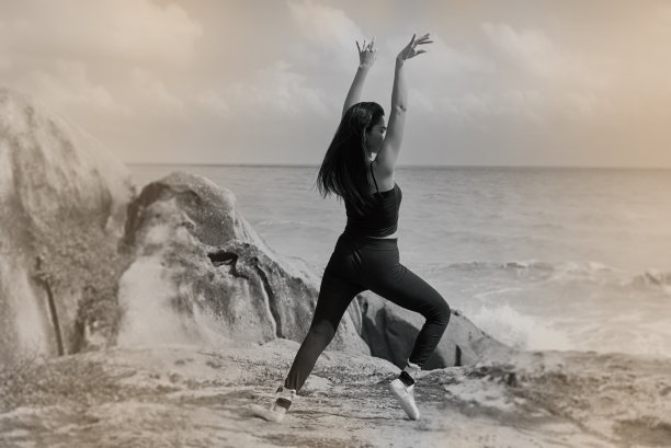 抽象的艺术设计背景，美女穿着黑色套装和缎子芭蕾舞鞋，在沙滩上摆出芭蕾舞图案，复古和艺术色调。图片下载