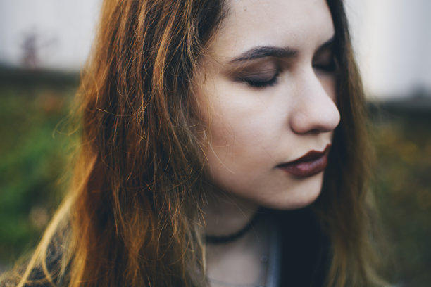 闭着眼睛的梦幻女孩站在街道上，模糊的彩色背景。黄色的阳光照在棕色的身上。电影般的镜头，体贴美丽的白人模特。图片下载