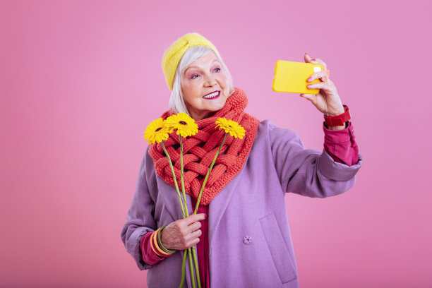 一名兴高采烈的退休妇女拿着黄色手机自拍图片下载