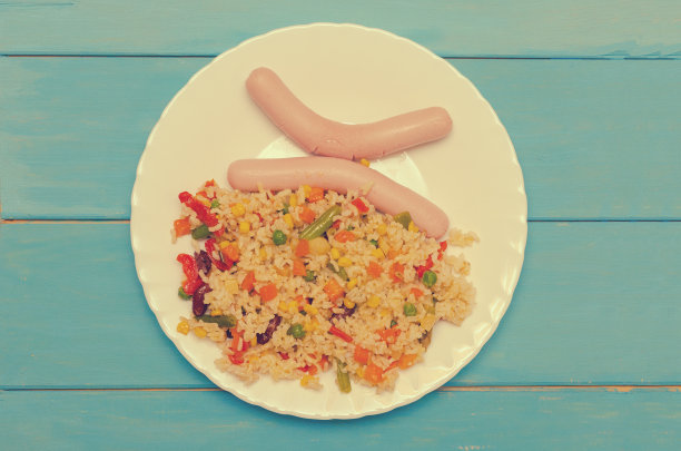白色盘子，两根香肠，米饭和蔬菜在蓝色的木制背景。图片下载