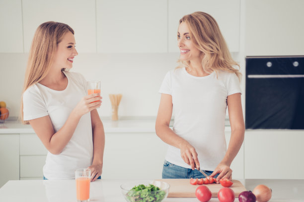 近距离的后面，后面，后视图照片两个人妈妈和十几岁的女儿最好的朋友一起做菜，在玻璃杯里，饮料，切西红柿，穿白色t恤，牛仔裤在明亮的平坦的厨房图片下载