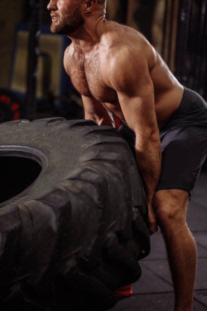近距离裁剪照片。肌肉发达的男人提轮胎有困难图片下载