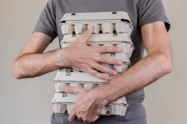 一个穿着灰色t恤的白人拿着四个装满鸡蛋的纸箱图片下载