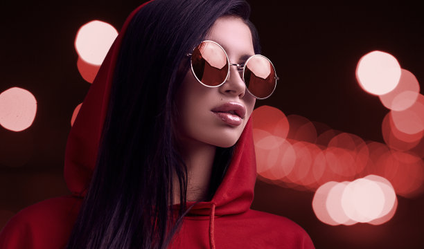美丽的黑发女人在夜晚的城市背景红色帽衫和眼镜图片下载