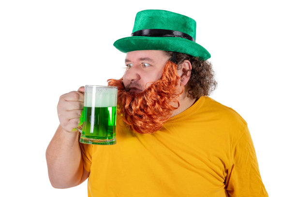 一个戴着矮妖帽、喝着绿色啤酒、面带微笑的胖男人在工作室里。他庆祝圣帕特里克图片下载