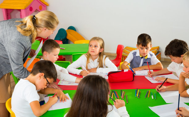 女教师在教室里帮助学生用彩笔画画图片下载