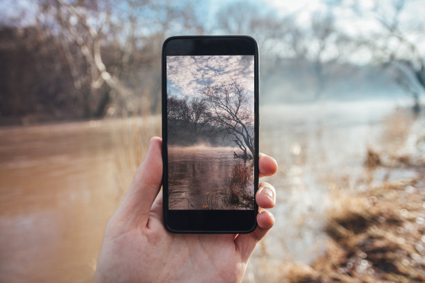 一名男子用智能手机拍摄清晨的雾和河流图片下载