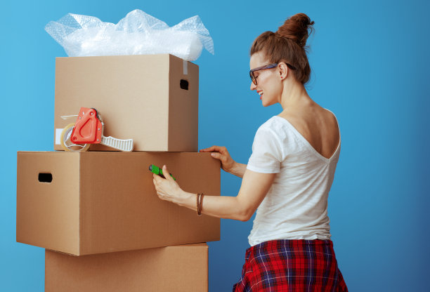 穿着白色t恤的现代女性在蓝色纸板箱上签名图片下载