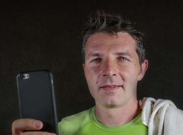 年轻快乐和有吸引力的30多岁或40多岁流汗的男人在健身俱乐部训练锻炼后微笑，在健身房锻炼时在手机上查看性能数据感到满意图片下载