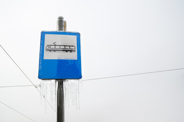 冬天，蓝色背景下的有轨电车车站的标牌上挂着冰柱，后面是阴天，电线向四面八方延伸。图片下载