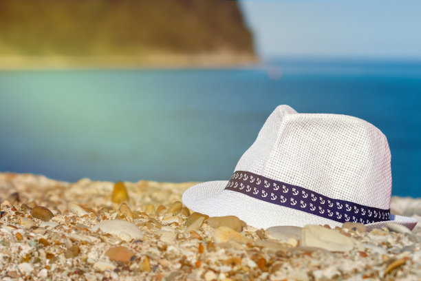 男人的白色帽子躺在石头上，以大海和山脉为背景。旅行者属性图片下载