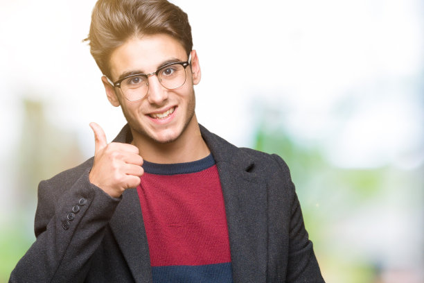 年轻英俊优雅的男子戴着眼镜在孤立的背景做快乐的拇指手势与手。赞许的表情看着镜头，表示成功。图片下载