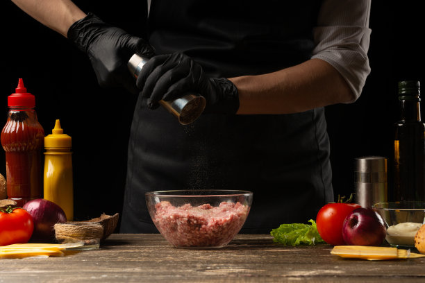 厨师用新鲜绞碎的牛肉来做汉堡中的肉饼。背景是汉堡的配料。水平的照片。烹饪美味的食物图片下载