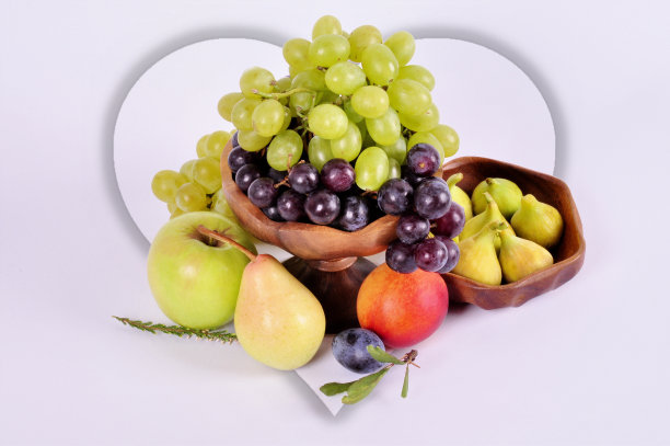木碗里装着浅色和深色的葡萄，白色背景上有苹果、梨子、李子和无花果。水果静物图片下载