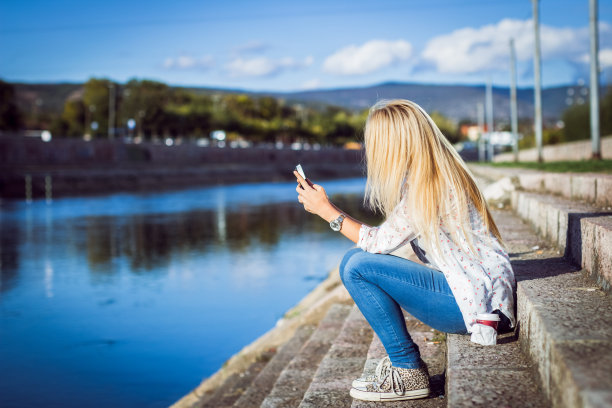 河边拿着手机的金发女孩图片下载
