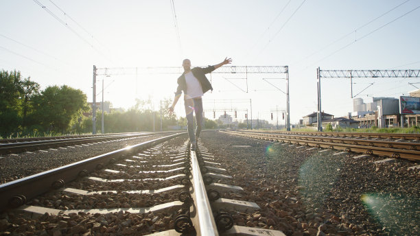 在铁路上行走的年轻人。保持平衡。摇滚风格。图片下载
