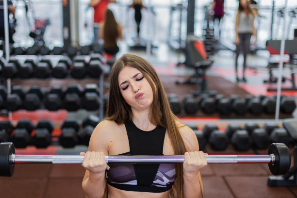 美丽的女孩在健身房的地板上用杠铃锻炼肱二头肌图片下载