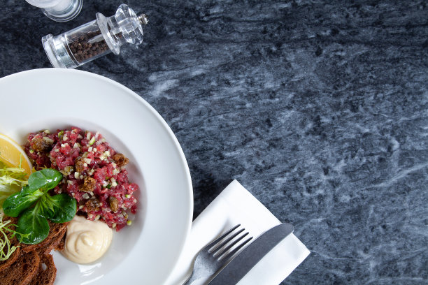 近距离观看牛排牛肉鞑靼与柠檬，面包，酱汁和沙拉在大理石桌上。餐厅食物菜单，食谱照片与复制空间。图片下载