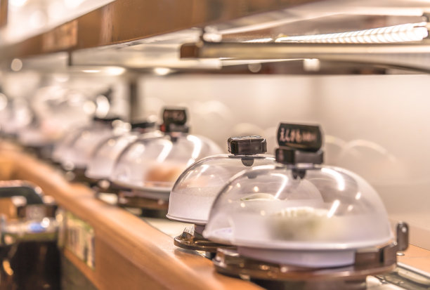 在日本传送带寿司餐厅的特写，盘子与寿司被放置在一个旋转的轨道上，保护与一个透明的塑料盖。图片下载