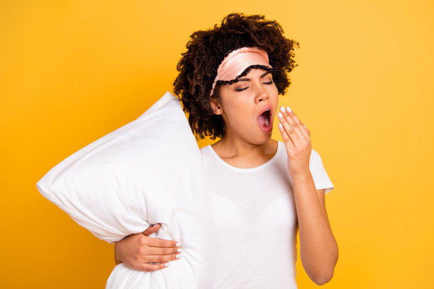 近距离的照片美丽的惊人的她，她的黑皮肤的女士，手打哈欠，拥抱，拥抱枕头，醒来，努力，早，穿睡眠面具，休闲的白色t恤，孤立的黄色明亮，充满活力，生动的背景图片下载