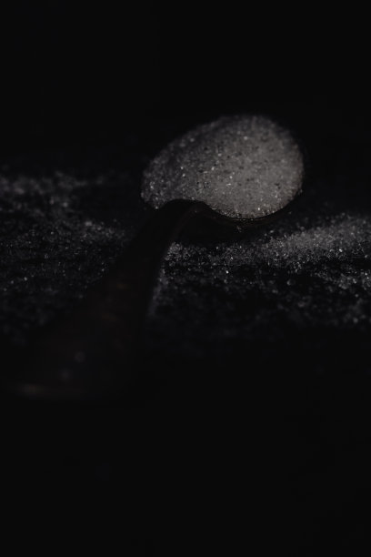 一张黑色的照片，汤匙与白糖在一个黑色的石头背景与复制空间，水平的视野，低关键照明图片下载