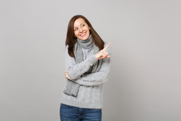 年轻女子在灰色毛衣，围巾指向食指一边孤立的灰色墙壁背景在工作室。健康时尚的生活方式，人们真诚的情感，寒冷的季节理念。模拟拷贝空间。图片下载