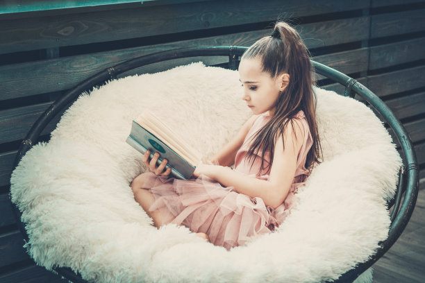 穿着粉红色连衣裙的少女坐在白色毛皮格子椅子上读书图片下载