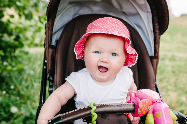 快乐的女孩在婴儿车玩在婴儿车的背景自然。描绘可爱的6个月小女孩坐在或婴儿车和等待妈妈。图片下载