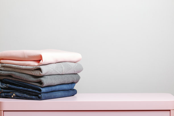 粉红色的桌子上放着一叠叠好的衣服。灰色的背景。特写镜头图片下载