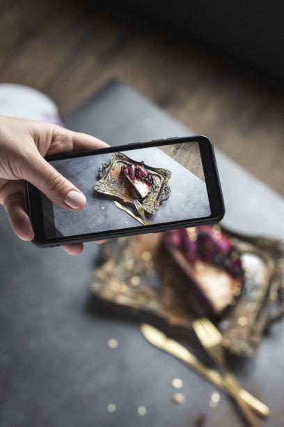 蛋糕和餐具的照片在手机上。一个女性的手与美丽的美甲。灰色背景图片下载