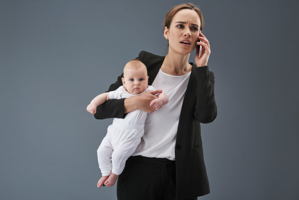 漂亮的妈妈一边打电话一边抱着她的孩子图片下载